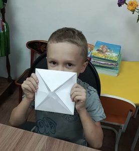 мальчик держит сложенную из бумаги заготовку